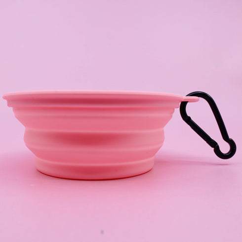 A pink collapsible silicone dog water bowl is displayed against a light pink background. It features a black carabiner clip for easy attachment, showcasing its practical and portable design for pet owners on the go.