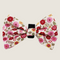 A floral bow tie featuring a white background adorned with vibrant pink, red, and yellow flowers. The bow tie has a velcro strap for easy attachment to any collar, showcasing a charming and playful design perfect for special occasions.