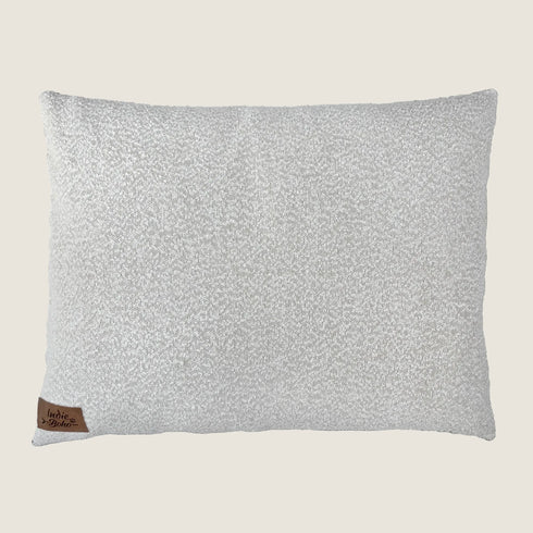 A soft, textured dog bed pillow in a neutral bouclé fabric featuring a light sage color. The bed has a small leather tag with the brand name Indie Boho stitched on one corner, adding a touch of elegance to the design.