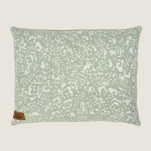 A rectangular dog bed featuring a soft sage green fabric adorned with a white floral and leaf pattern. The bed has a small tag in the lower corner that reads Indie Boho, emphasizing its stylish and cozy design.