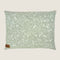 A rectangular dog bed featuring a soft sage green fabric adorned with a white floral and leaf pattern. The bed has a small tag in the lower corner that reads Indie Boho, emphasizing its stylish and cozy design.