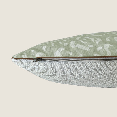 Close-up view of a dog bed featuring a textured bouclé fabric in neutral tones, with a sage green top displaying abstract brushstroke patterns. The design includes a zipper along one side for easy removal and cleaning of the cover.