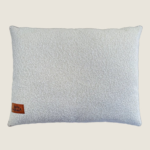 A plush, rectangular pillow featuring a soft, textured bouclé fabric in a light cream color. The pillow includes a small brown label with the brand name Indie Boho stitched on one side.