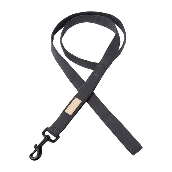 A sleek, dark gray dog lead made from soft, textured cotton lies flat against a white background. It features a matte black metal clasp and a small beige label, showcasing its minimalist and refined design.
