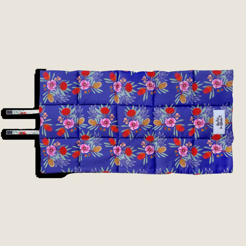A vibrant dog travel mat featuring a bold floral pattern with purple flowers, red accents, and green foliage set against a rich blue background. The mat is designed with straps for easy carrying and is perfect for outdoor adventures.