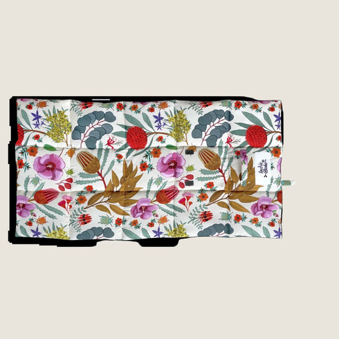 A vibrant dog travel mat featuring a colorful illustration of Australian wildflowers, including pink orchids and green foliage, set against a white background. The mat is folded and displays a mix of botanical designs.