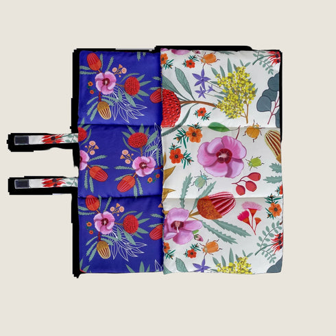 A colorful dog travel mat featuring vibrant illustrations of various flowers and plants, with a distinct blue side adorned with bold floral patterns and a contrasting white side showcasing a different array of colorful botanical designs.