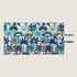 A colorful reversible travel mat featuring a vibrant coastal pattern with palm leaves in shades of blue, green, and orange. The mat has a quilted design and includes two fabric loops for easy storage or attachment.
