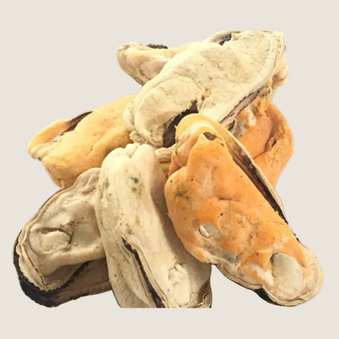 A pile of freeze-dried green lip mussels in various shades of beige and orange is displayed against a neutral background. These treats are shaped like mussel shells, showcasing their unique textures and colors.