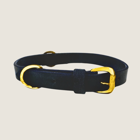 A navy leather collar with a minimalist design features a shiny gold buckle and two gold rings. The collar is simple yet elegant, showcasing a classic look suitable for various occasions.