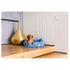 A small dog is comfortably lying in a light blue corduroy pet bed, positioned on a wooden floor beside a large, sculptural gold decor piece. The modern interior features a minimalist design with textured walls and warm lighting.