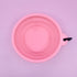 A pink collapsible silicone dog water bowl is displayed against a light purple background. The bowl features a clip for easy attachment, showcasing its practical design for travel and outdoor adventures.
