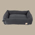 A plush, slate grey corduroy dog bed features high padded sides and a soft interior, designed for comfort. The bed has a simple, elegant shape and a small label on one side.