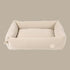 A plush, beige corduroy pet bed with a rectangular shape and softly padded sides, designed for comfort and style. The bed features a smooth interior and a subtle logo tag on one side.
